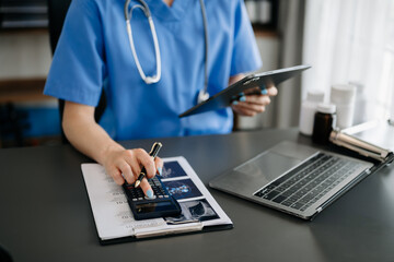 Healthcare costs and fees concept.Hand of smart doctor used a calculator and smartphone, tablet for medical costs at hospital in morning light