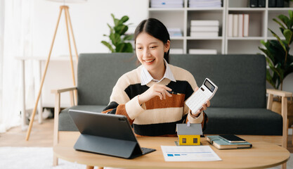 Young real estate agent worker working with laptop and tablet at table in home office and small house beside it.