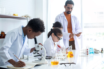 Elementary school classroom, African American boy in Lab coat intend in chemistry class, group of multiethnic kids science lab, selective focus