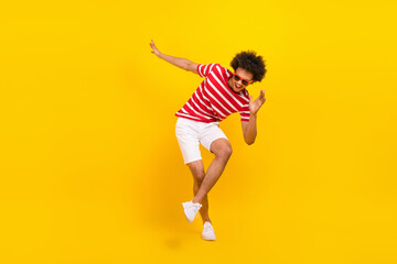 Fototapeta na wymiar Full length photo of cool good mood man wear striped t-shirt dark spectacles dancing having fun isolated yellow color background