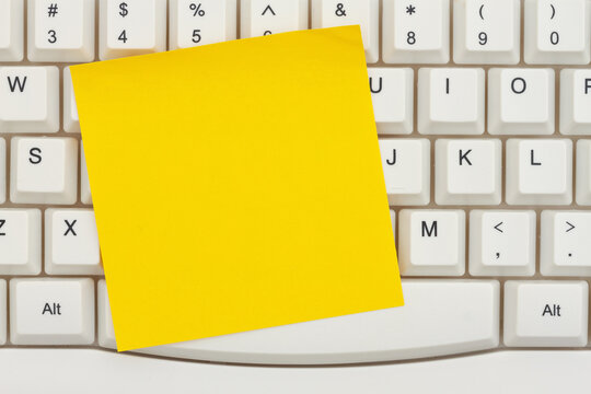 Blank yellow sticky note on a gray computer keyboard