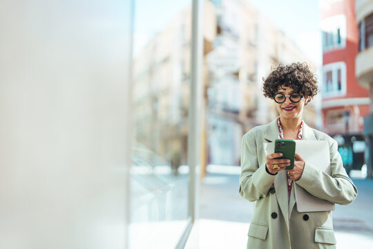 Woman texting with smartphone outdoors. Beautiful Fashionable Woman is Walking Down the City Streets and Using a Smart Phone to Communicate with her Friends or Colleagues.