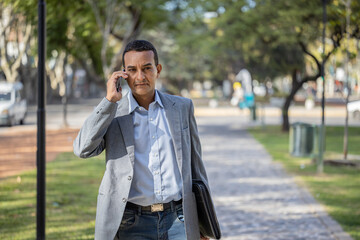 Young latin man in suit walking and talking on mobile phone with copy space.