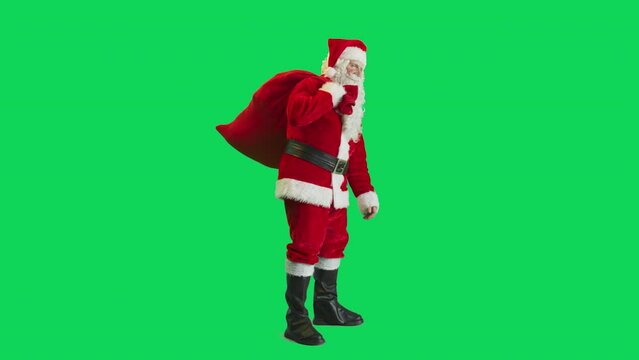 Studio Shot Isolated Mockup Template: Jolly Santa Claus Picking Up Bag With Gifts For All Good Children On Green Screen Chromakey Background And Waving To Camera In Slow Motion. Christmas And New Year