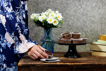 closeup woman holding a homemade chocolate muffins in stand cake with daisy flowers vase