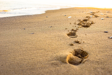 Footprints on the sand with background of blured flat sea weaves.