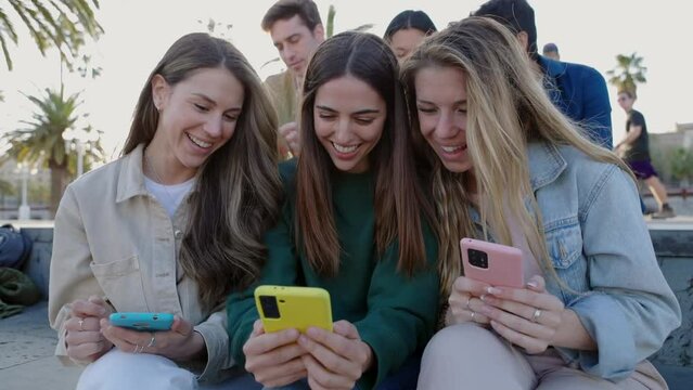 Young group of pretty women having fun using smart mobile phones together outdoors. Addicted millennial student friends using smartphones to watch social media content sitting together in city street.