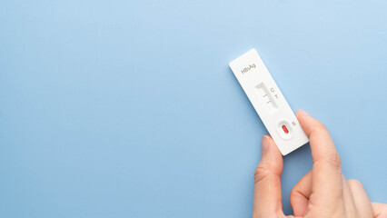 Hand holding Hepatitis B Virus Surface Antigen Test Kit with positive result on blue background. Screening for hepatitis B uses a blood sample, collected from a finger prick. World hepatitis day.