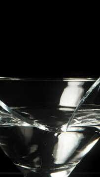 A broken martini cocktail glass on a black background, dolly slider extreme close-up. Vertical video.