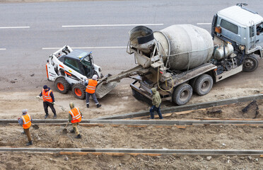 Team of road workers in orange signal vests transfer concrete from concrete mixer truck into mini...