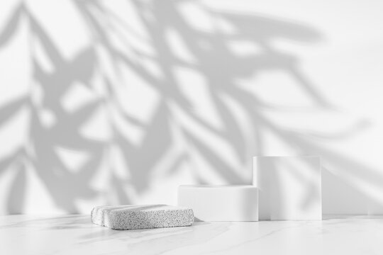 Minimal white scene for cosmetic product presentation made with empty white podiums on white background with leaves shadow.