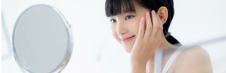 Beautiful face of young asian woman with happy smiling and touch cheek looking mirror with...