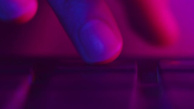 Close-up of a electronic musician clicks the pads at the controller with hands making the beat during the studio recording session in a color violet light