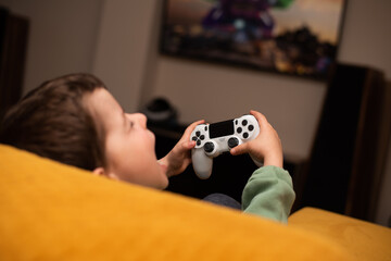 A little boy plays games on a game console with a gray joystick © volkonskaya