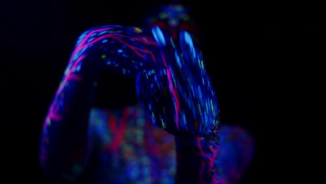Mysterious artistic girl in acid fluorescent neon painting with UV abstract makeup dancing contemporary dance, dark background in studio