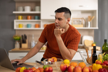 Fototapeta premium A homely and healthy male prepares nutritious diet, including variety of fruits. Following cooking show on laptop Mastery of peeling, chopping, and slicing fruits to prepare them in artistic style.