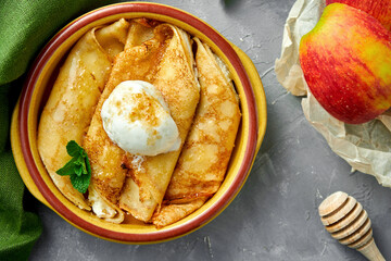 Pancake rolls stuffed with apple and sour cream in a clay bowl on a gray background. Blini, stuffed crepe