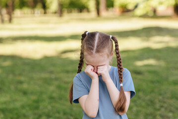 Portrait of an angry, sad and crying little girl in nature in pacre, Emotions of a child when he throws a tantrum and gets angry, an expression of grumpy emotion. 