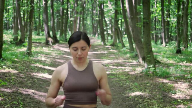 Attractive sporty woman running outdoors in a summer park and checking pulse, time or pace on her smart watch. female jogging in the morning forest. Healthy lifestyle concept