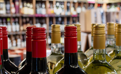 Red and golden caps of wine bottles close-up on blurred background of wine shelves