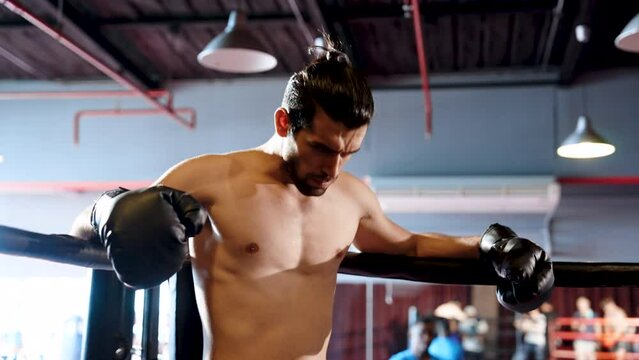 Close-up young athlete who specializes in boxing, leaning against long string on boxing ring exhausted during sparring time, man breathing heavily, in mouth wear boxer teeth prevent broken teeth.