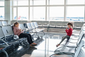 Children, kids, girls waiting for plane flight in departure hall. Sitting on chairs, playing...