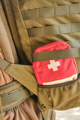 Naklejka premium A red first aid kit with a white cross in the pocket of a tactical military olive backpack with a Molle system