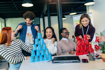 Group of young business people playing, building towers from plastic cups, two teams, blue and red. Teambuilding activity.