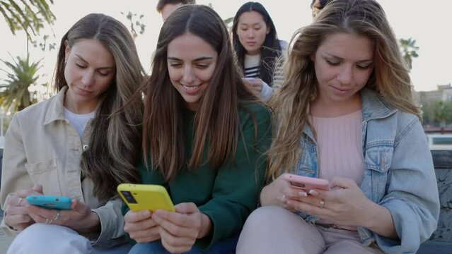 Happy young group of student friends using mobile phones outdoors. Multiethnic millennial people having fun watching social media content on network app platform on cellphone.
