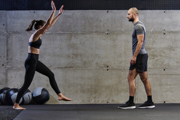 A muscular man assisting a fit woman in a modern gym as they engage in various body exercises and muscle stretches, showcasing their dedication to fitness and benefiting from teamwork and support