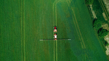 Aerial  view of tractor spraying pesticides on wheat  field with sprayer  in spring. - obrazy, fototapety, plakaty