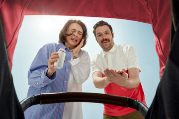 Emotional parents, young man and woman looking into baby carriage during walk outdoors on warm sunny day. Concept of parenthood, family, emotions, care, happiness