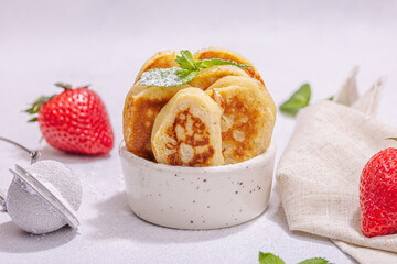 Cottage cheese pancakes, syrniki, curd fritters with strawberry, mint and powdered sugar in a bowl