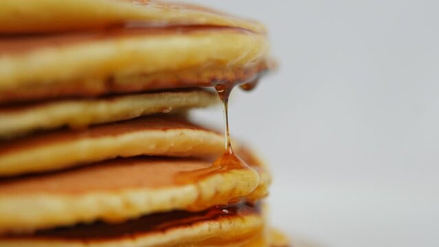 Close-up honey drops falling on side of pile of crepes in slow motion. Extreme close up delicious tasty dessert at white background on the left