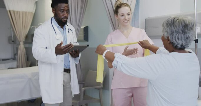 Diverse male doctor talking with happy female physiotherapist and senior female patient, slow motion