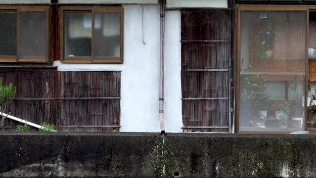 Water flows from drain pipe on historic wooden Japanese house in rain