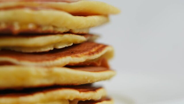 Closeup pancakes with honey syrup spinning in slow motion on the left. Tasty sweet dessert turning at white background close-up