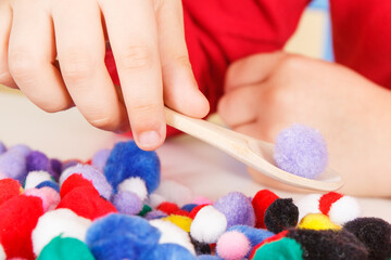 Little baby boy playing with small pompoms, wooden spoon and cups. Development of kids motor...