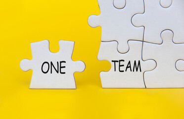 One Team text on separated jigsaw puzzle on yellow background. Teamwork concept