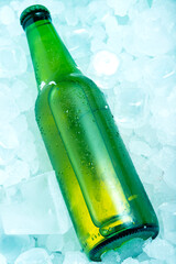 Bottle of green beer in ice cubes very cold in vertical