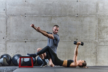 A muscular man assisting a fit woman in a modern gym as they engage in various body exercises and muscle stretches, showcasing their dedication to fitness and benefiting from teamwork and support
