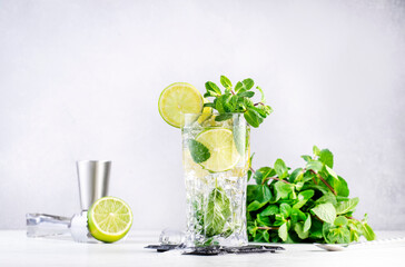 Mojito summer alcoholic cocktail drink with lime, white rum, soda, cane sugar, mint, and ice in highball glass on gray background.  Steel bar tools. Copy space
