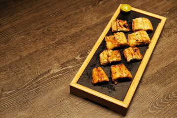 sliced grilled eel fish meat on plate on patterned wooden table. Traditional Japanese food