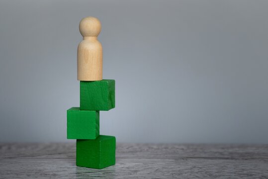 Doll Standing On Top Of Unstable Wooden Block On Table With Copy Space. Risk, Uncertainty And Challenge Concept