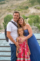 Happy parents with their daughter are standing at the handrails on the river bank