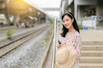Fototapeta premium young asian woman traveler with weaving basket waiting for train in train station. Journey trip lifestyle, world travel explorer or Asia summer tourism concept.