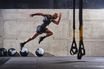 A muscular man captured in air as he jumps in a modern gym, showcasing his athleticism, power, and...
