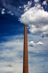 View of an ancient high chimney against the blue cloudy sky