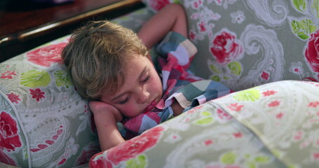 Child lying napping on sofa. Tired toddler slouched on couch sleeping