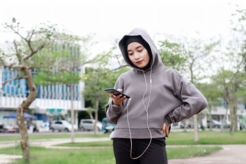 Asian young muslim women using phone after doing stretching exercise at city park